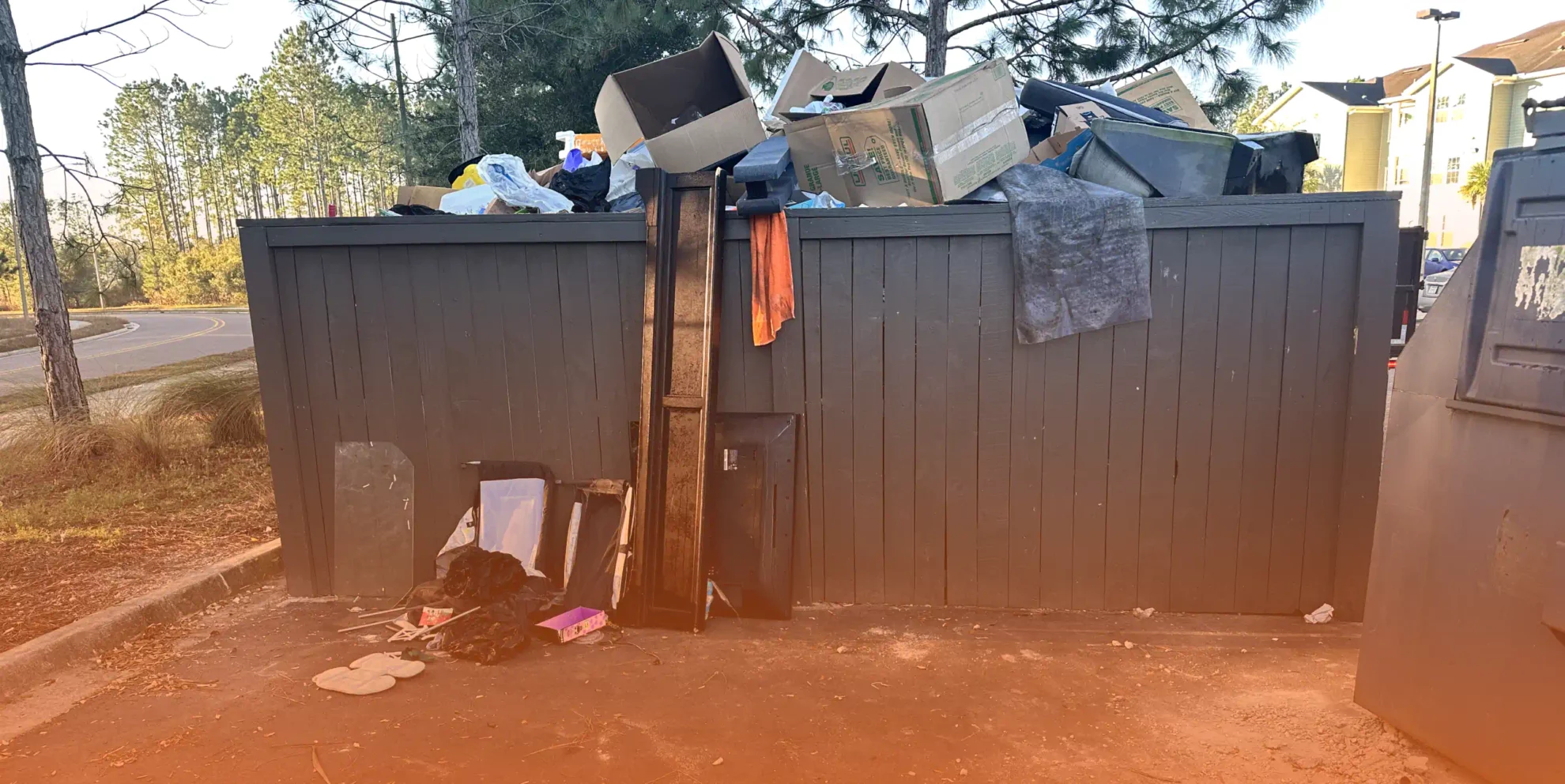 grey dumpster with cardboard boxes innside and trees around